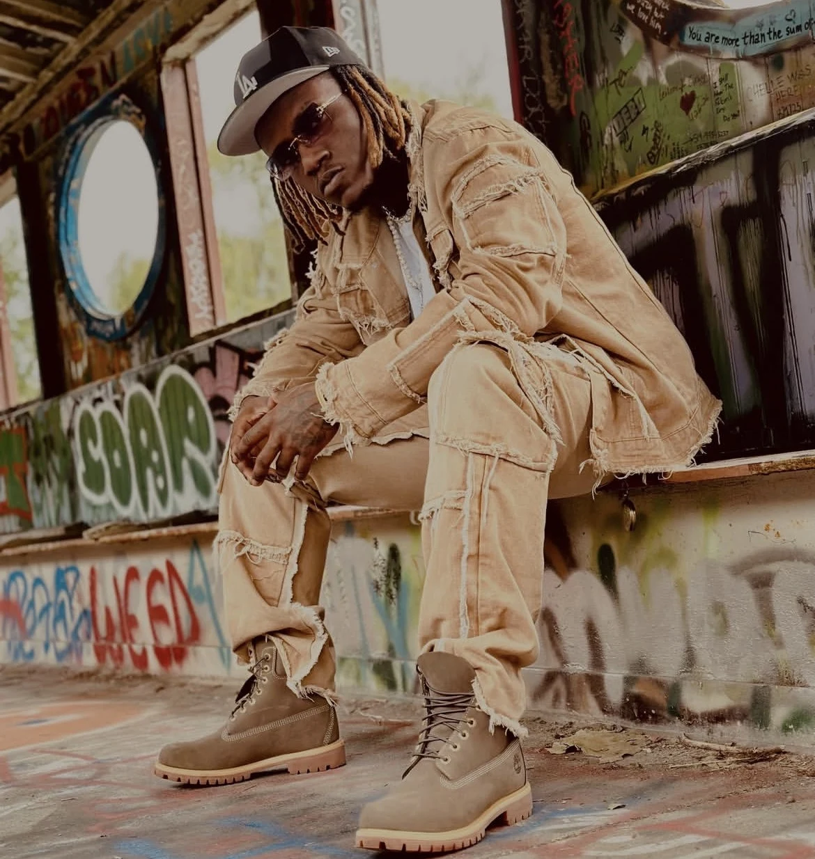 Kameron Ingram in distressed tan denim and boots, seated in a textured industrial interior.